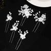 A set of white pearl flower bridal hair clips with silver accents displayed on a black surface.