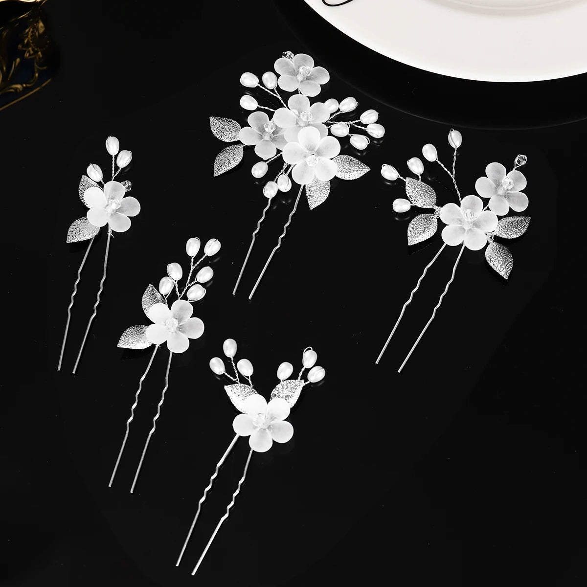 A set of white pearl flower bridal hair clips with silver accents displayed on a black surface.