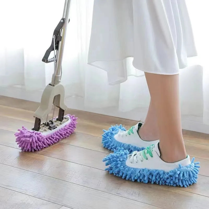 A person's foot wearing a blue fuzzy slipper is positioned on a wooden floor next to a mop and cleaning tools.