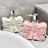 A pink ceramic pump dispenser bottle with a bowknot design sits on a gray countertop next to a white sink.