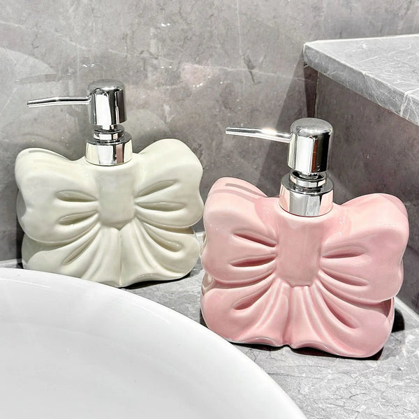 A pink ceramic pump dispenser bottle with a bowknot design sits on a gray countertop next to a white sink.