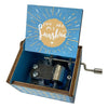 A mini wooden music box with a blue lid featuring a sunburst design and an open side showing the internal mechanism.