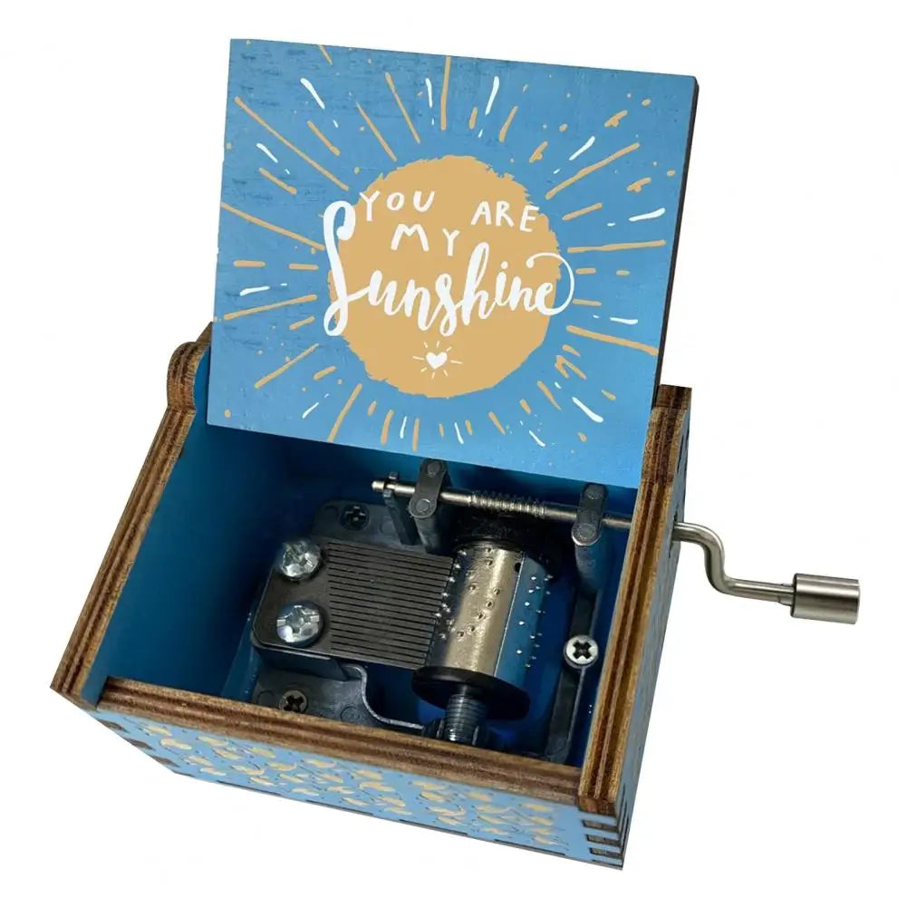A mini wooden music box with a blue lid featuring a sunburst design and an open side showing the internal mechanism.