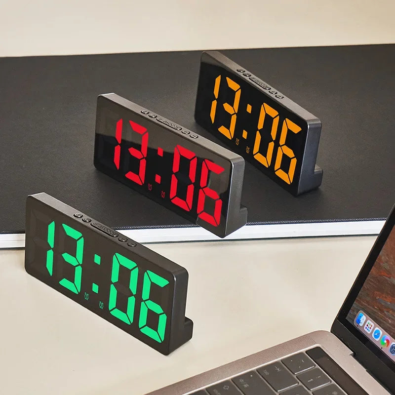 Three digital alarm clocks displaying 13:06, with one in red and two in green, resting on a dark surface.
