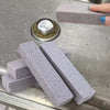 Two gray pumice stone sticks are displayed on a metal surface with a metal disc.