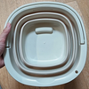 A white collapsible water bucket with a handle is shown being held by a hand.
