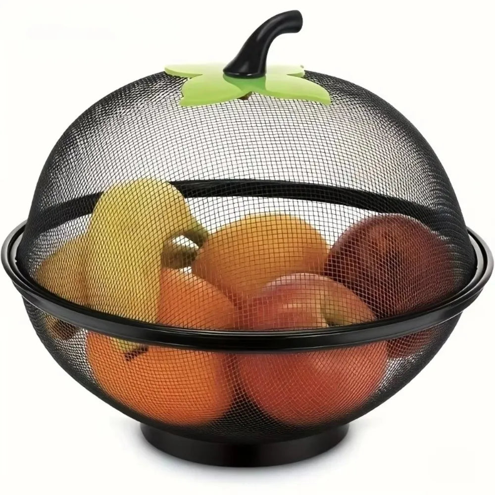 A black metal fruit basket with a mesh cover holding various fruits and topped with a green leaf handle.