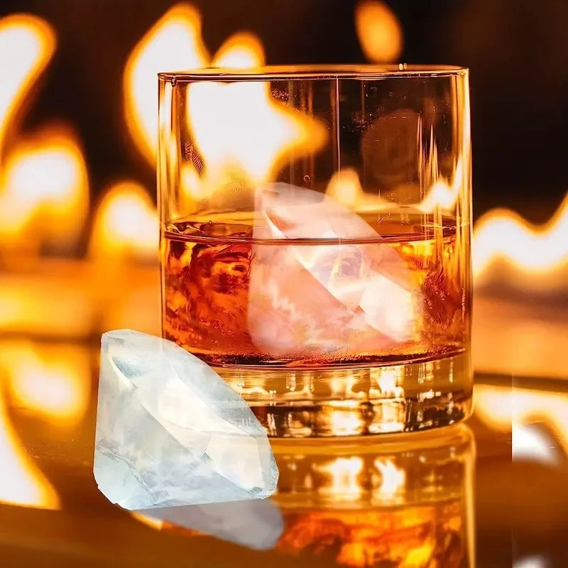 A glass of amber liquid sits in a square glass, with a clear ice cube resting inside and glowing against a warm fire backgrou