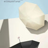 A black folding umbrella is shown casting a shadow on a white surface.