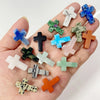 A collection of natural agate and jasper cross pendant charms in various shades of blue, green, and orange held in a hand.