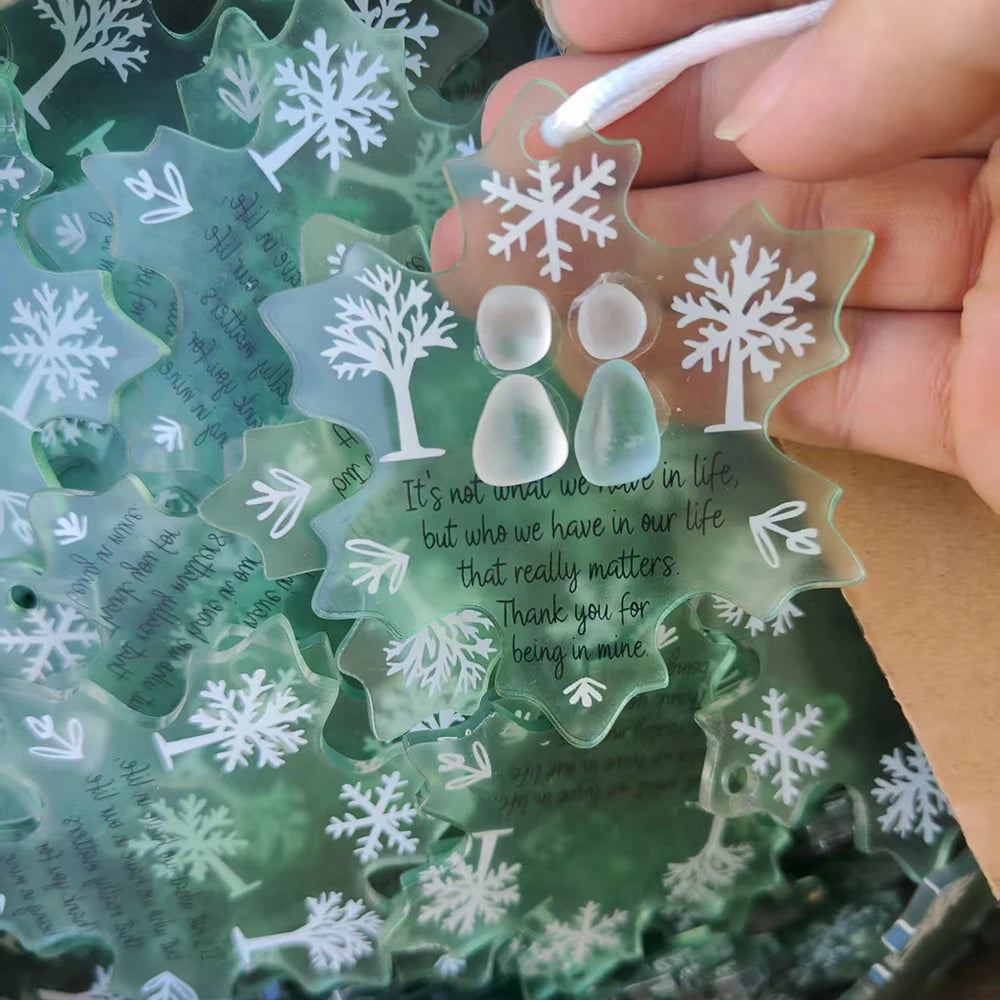 Une main tient un ornement de flocon de verre de mer fait main avec texte gravé et motif d'arbre.