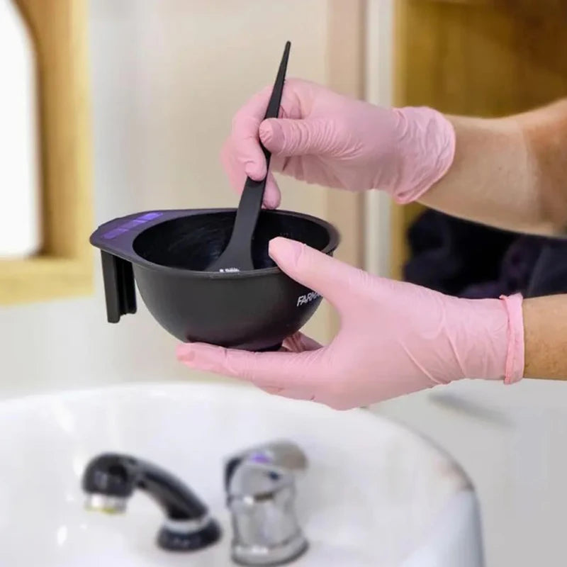 Hands in pink nitrile gloves are holding a black silicone pot with a black spatula over a white sink.