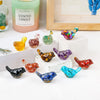 A collection of colorful crystal bird statues in various shades of green, purple, and orange displayed on a white surface.