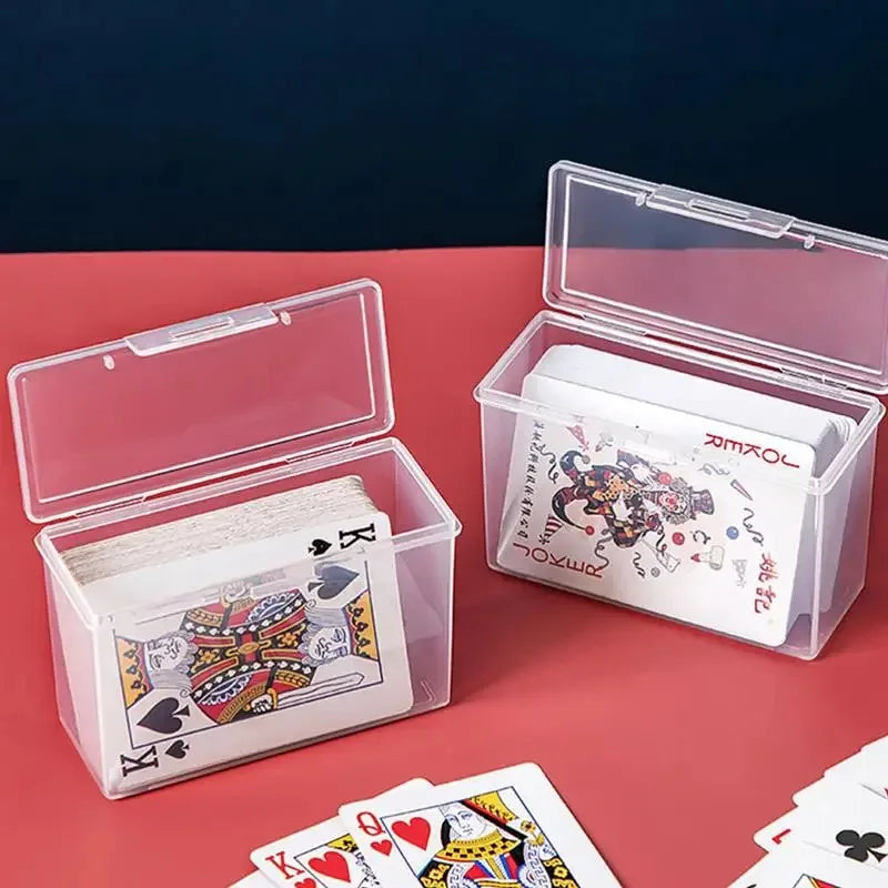 A clear plastic storage box with a lid holds playing cards and other small items on a red surface.