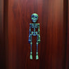 A set of luminous magnetic poseable skull fridge magnets in a dark teal color displayed against a wooden background.