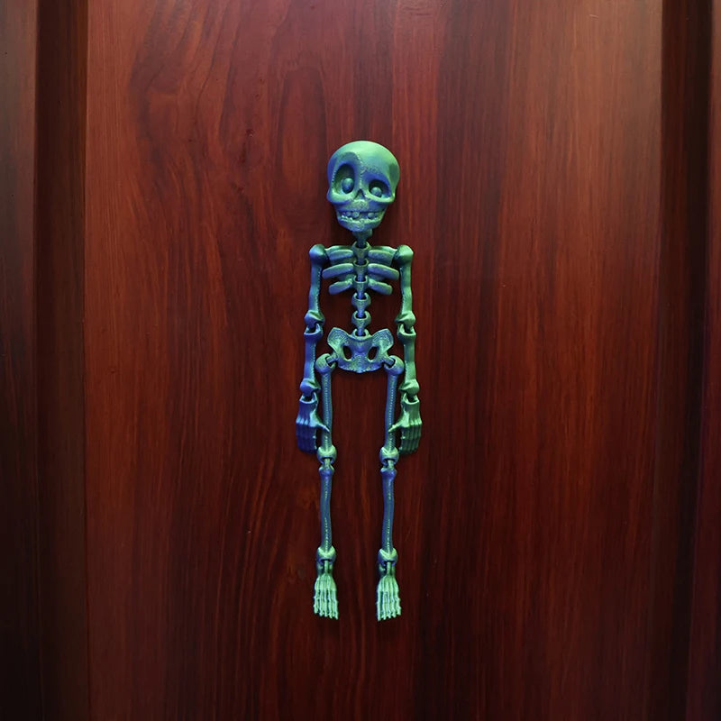 A set of luminous magnetic poseable skull fridge magnets in a dark teal color displayed against a wooden background.