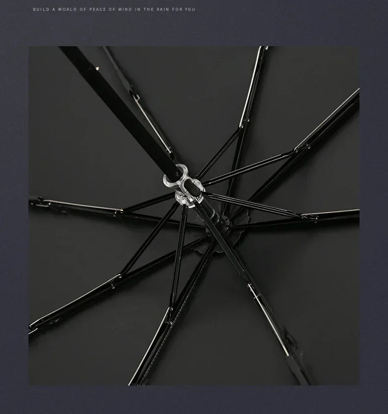 A black folding katana sword umbrella with a silver hilt is shown in a dark, overhead view.