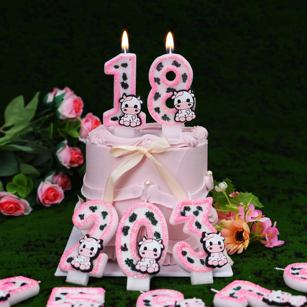 A pink birthday cake decorated with number candles spelling eighteen and twenty-three featuring cow print designs.