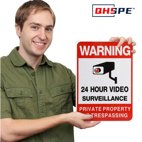 A man holds up a warning sign for 24 hour video surveillance and trespassing on private property.