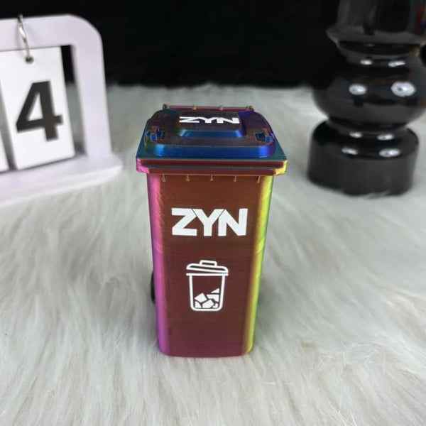 A small, colorful desk organizer trash can with a lid and wheels is shown on a light surface.