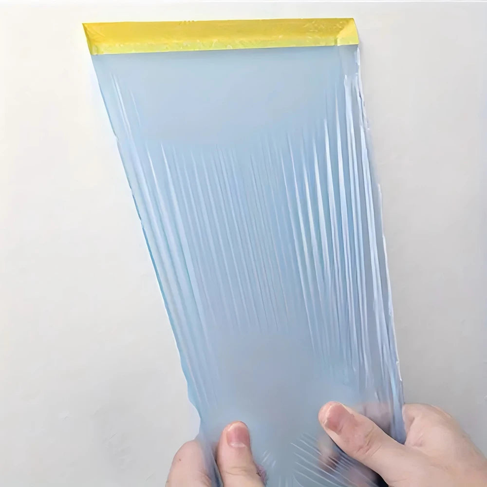 A hand holds a sheet of clear blue plastic masking film tape with a yellow edge.