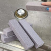 Several gray natural pumice stone cleaning sticks are displayed on a metal surface.