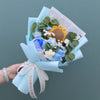 A handmade sunflower crochet bouquet wrapped in light blue paper with a white ribbon.