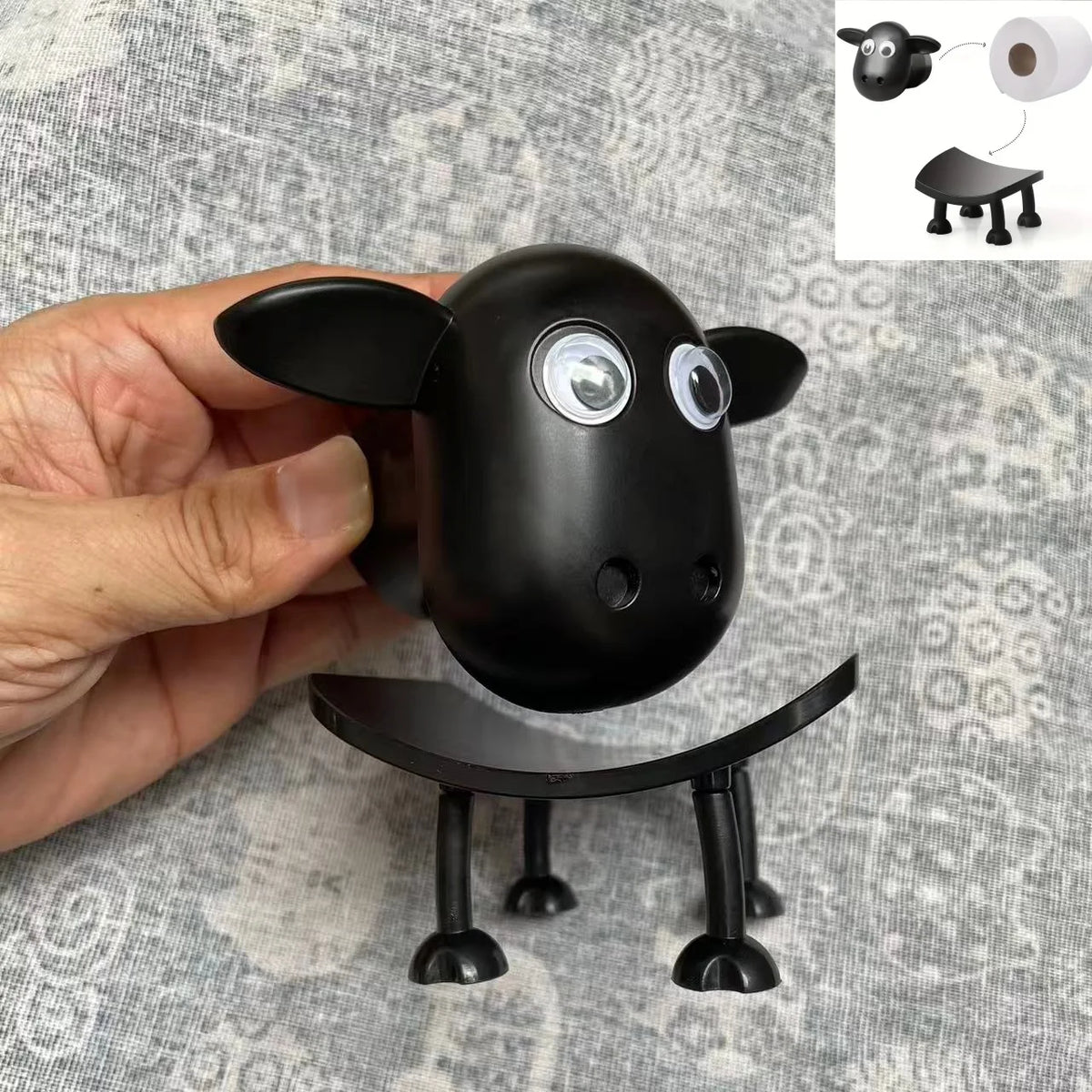A black decorative toilet paper holder shaped like a pig, shown being held by a hand.