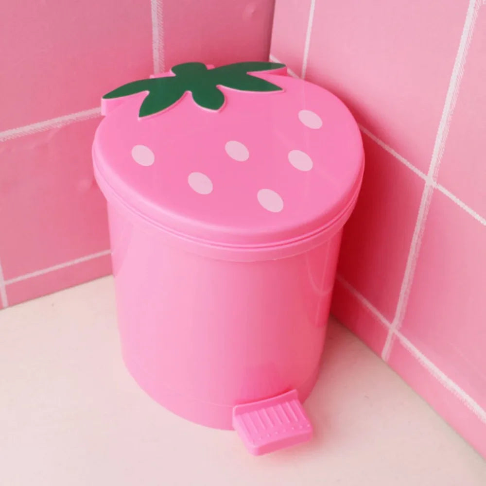 Pinkes wiederverwendbares Erdbeer-Dekor-Mülleimer mit grünem Blatt, vor pinker Fliesen-Hintergrund.