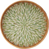 Round rattan serving tray with mother of pearl inlay featuring a pattern of green leaves.