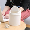 A white compact desktop trash can with a flip cover sits on a wooden table next to a laptop.