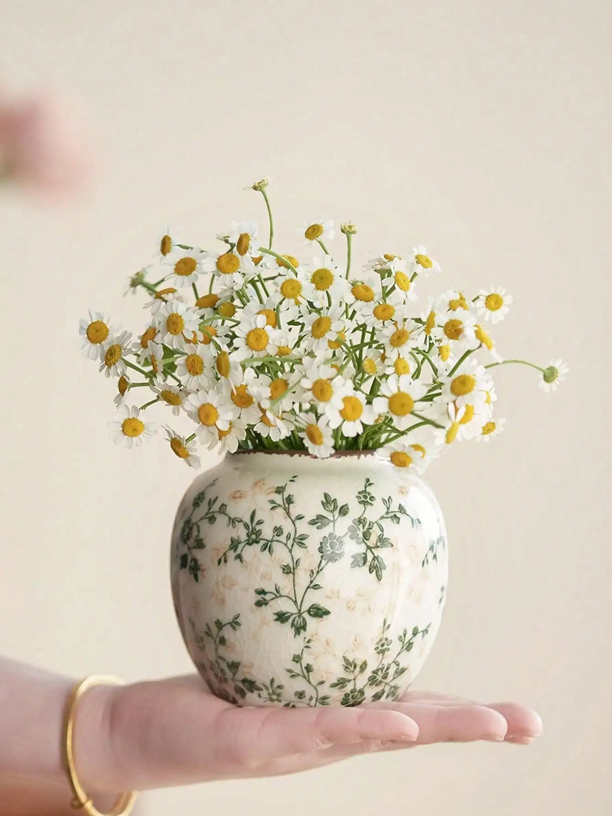 A hand holds a white ceramic bud vase filled with yellow and white wildflowers.
