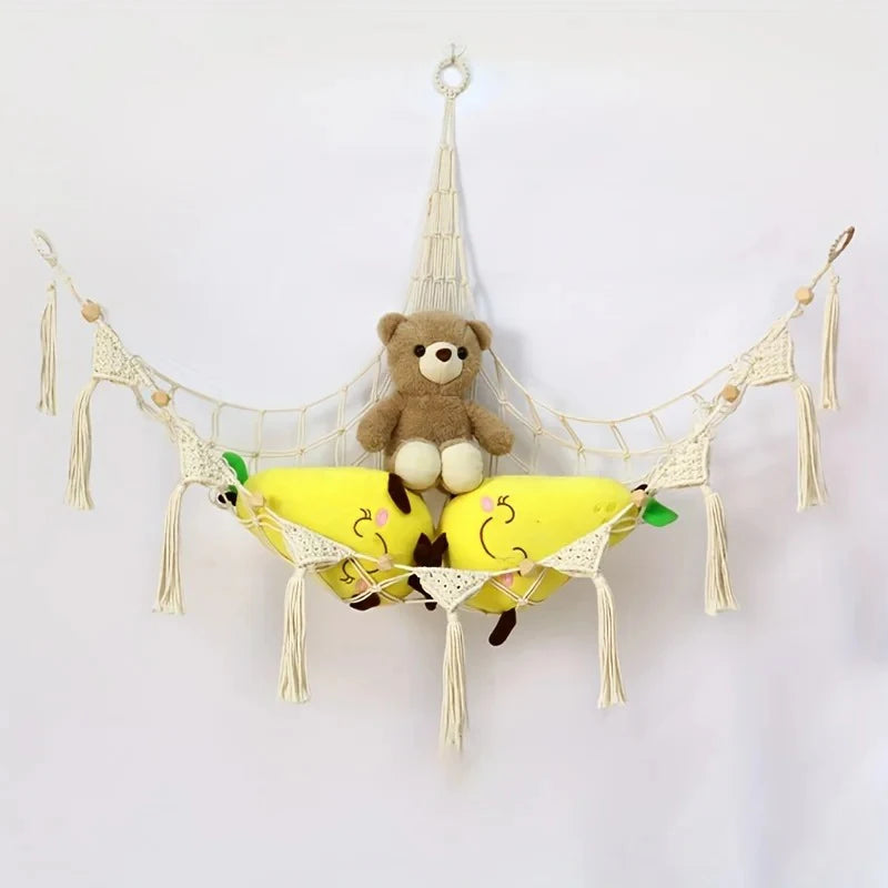 A plush bear hangs from a woven net hammock decorated with yellow fruit shapes.
