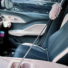 A pink fluffy duster brush is shown resting on the interior of a car, near a seat.