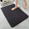 A black, textured 3D non-slip bathroom doormat placed on a light gray floor.