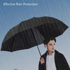 A man holding a sturdy black umbrella in the rain against a blue sky background.