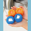 A hand holds three colorful cleaning balls—orange, blue, and white—used for washing machine cleaning.