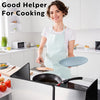 A woman wearing an apron is preparing food on a stovetop with a foldable stainless steel oil splash guard.