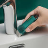A hand holds a teal reusable household stain remover eraser, applying it to a white ceramic surface.