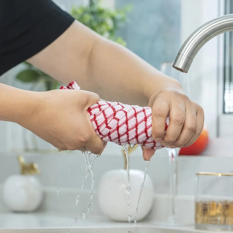 A hand is using a red absorbent cotton cleaning cloth to wipe down a surface.