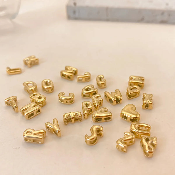 A collection of gold-plated 3D bubble letter alphabet charms scattered on a white surface.