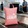 A pink laundry bag with a white graphic of an airplane and clouds is placed on a metal conveyor belt.