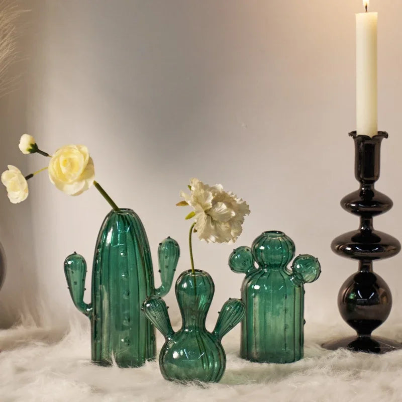 Collection de vases en cactus en verre vert présentés sur du tissu de fourrure blanche sur fond clair.