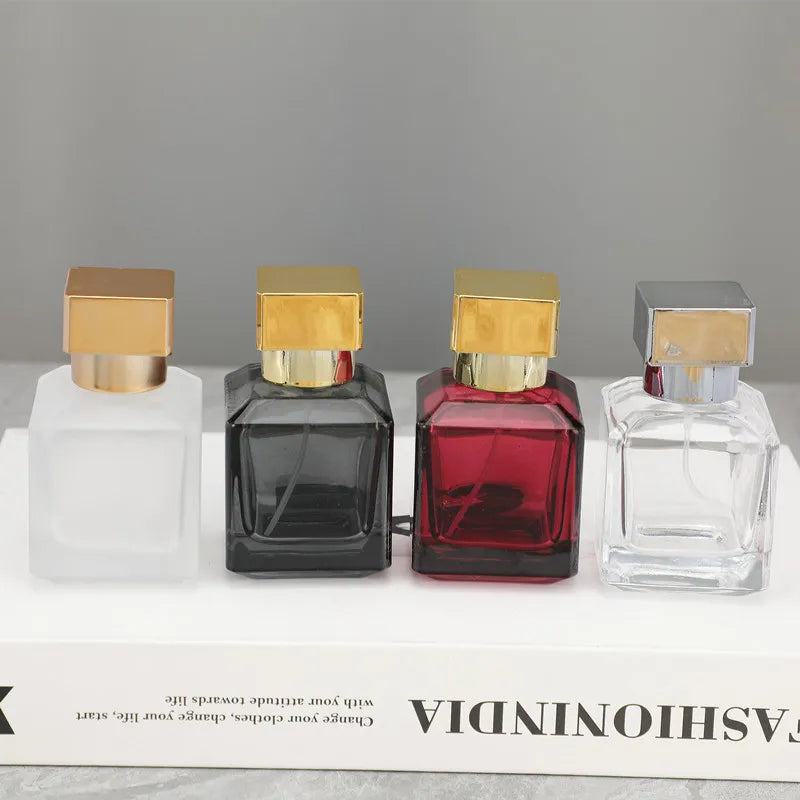 Three glass perfume bottles in various colors and shapes displayed on a white box.