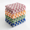 A stack of plaid cotton bath towels in various colors including pink, orange, and green.