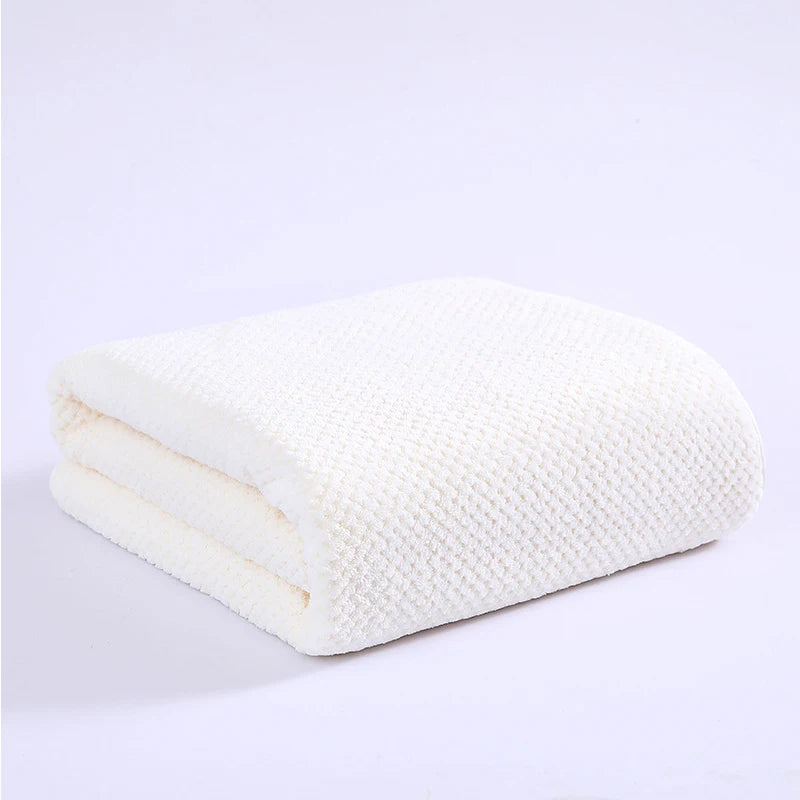 A stack of thick white microfiber bath towels folded neatly on a white surface.