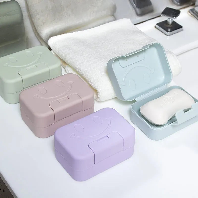A set of aesthetic ceramic soap dishes in pastel colors with lids and a white towel on a white surface.