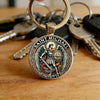 A silver keychain featuring an engraved design of Saint Michael the Archangel protecting us.