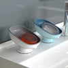 A set of light blue and gray suction cup soap dishes with built-in drainage sitting on a white countertop.