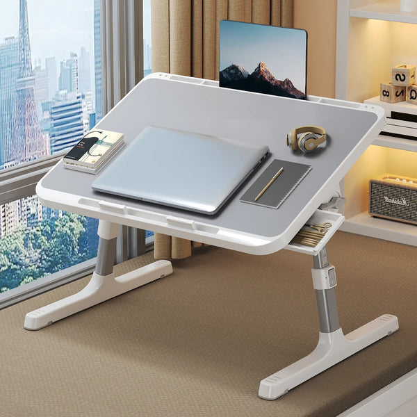 A white adjustable wooden laptop tray with a built-in stand holding a silver laptop, a tablet, and headphones.